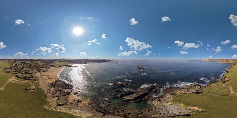 Vista panorámica de la Playa de Verdicio o Tenrero, en Gozón, con el sol brillando en un cielo despejado. Se aprecia la amplitud del arenal, los acantilados que la rodean y la vegetación costera característica del litoral asturiano.