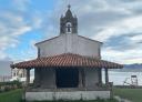 Small white chapel with bell tower, surrounded by lawns and sea views.