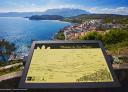 Yellow information panel on coastal landscape of village and blue sea