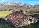 Old stone building with a reddish roof and a mountain range in the background.