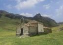 Small stone chapel with bell tower surrounded by green meadows and nature.
