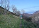Two hikers walk along a mountain path overlooking the valley