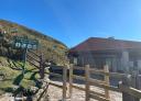 Visitor centre with information sign and stone building in a hilly environment