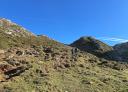 A couple of hikers ascending a mountainside under a blue sky.
