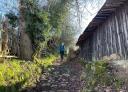Hiker walking along a stretch of cobbled path with a wooden building on one side of the path.
