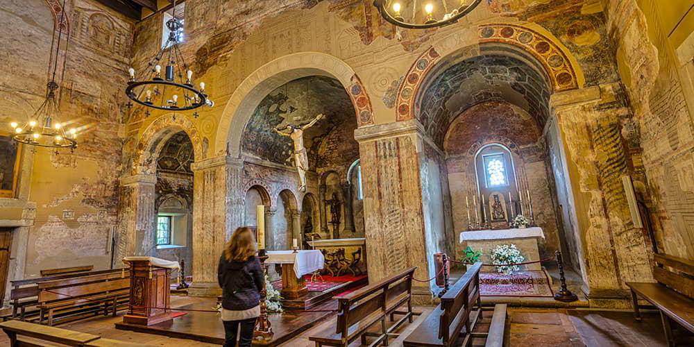 A woman with her back to the main altar of San Julián de los Prados, surrounded by its historic wall paintings.