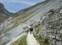 A couple of hikers walk along a stone wall.