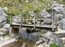 Wooden footbridge crosses small stream in rocky environment