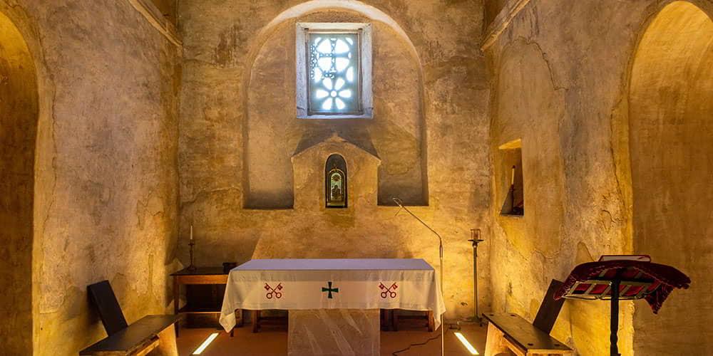 Interior of the church of San Pedro de Nora, showing the altar, the wooden pews and the small niche in the wall.
