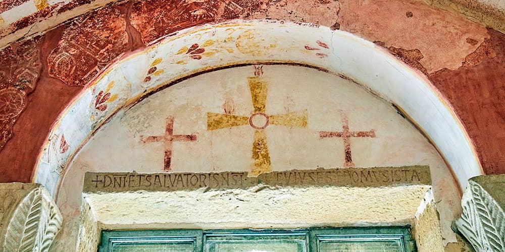 Paintings of three crosses over a Latin inscription inside San Salvador de Valdediós.