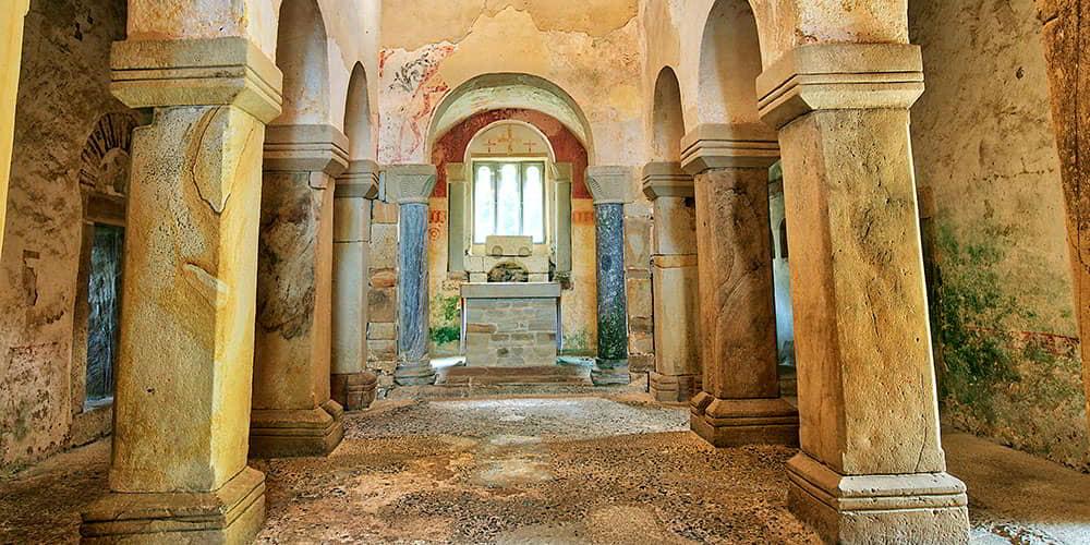 Interior of the church of San Salvador de Valdediós with its columns of decorated capitals and the altar in the background.