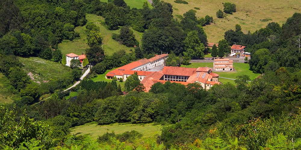 Aerial view of the Monumental Complex of Valdediós surrounded by lush vegetation.