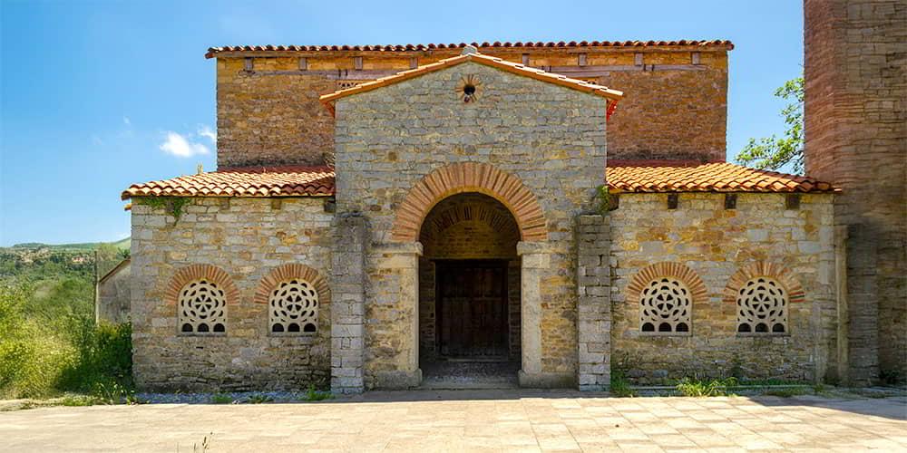 Detail of the main entrance of the pre-Romanesque church of Santa María de Bendones, highlighting the windows with round arches and latticework.