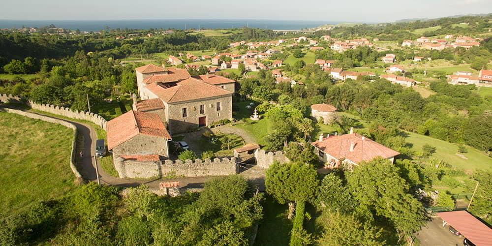 A landscape of Asturias showing Gobiendes Palace and the nearby village, in a rural setting overlooking the sea.