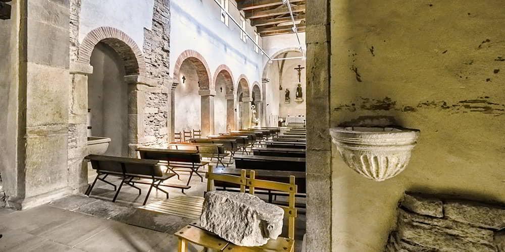 View of the nave of the church of Santiago de Gobiendes, showing the pillars, arches and baptismal font in the foreground.