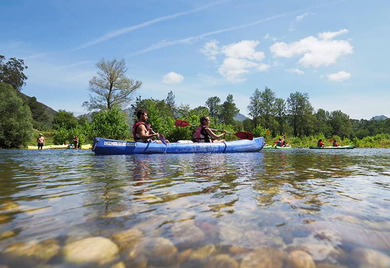 Two people paddling in a blue kayak on the river Sella in Asturias, with the clear water showing the rocks at the bottom.