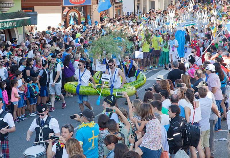 A parade or passacaglia during the Fiesta del Descenso del Sella in Arriondas/Les Arriondes, with costumed participants and a crowd.