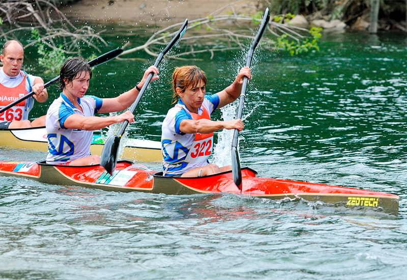 A women's canoeing team in action in the Descent of the Sella, with water splashing around the paddles.