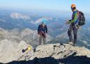 Mountaineers prepare to descend a steep rocky ridge in safety gear.