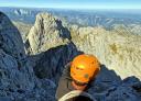 A climber in an orange helmet looks down on the view from the top of a mountain.