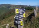 Trail sign with directions in mountainous landscape with lush vegetation and blue sky