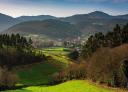 Green valley with village in the distance, surrounded by mountains and dense vegetation.