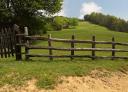 A dirt road borders a green meadow with a rustic wooden fence.