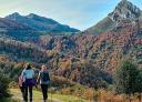 Three hikers walk along an autumn trail surrounded by mountains and trees.
