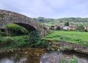 A stone bridge crosses a stream into a village