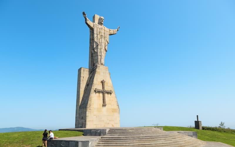 Monumento al Sagrado Corazón de Jesús en el monte Naranco, Oviedo, visto de frente sobre las escaleras, con la cruz en la base y bajo un cielo azul despejado.