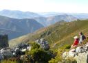 A mountaineer rests on rocks in a vast, undulating mountain landscape.
