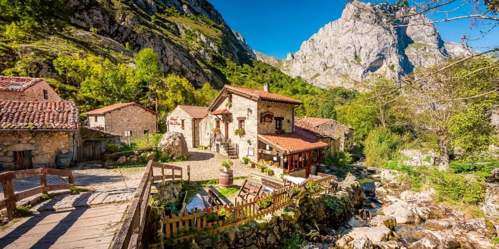 Vista panorámica de la aldea de Bulnes, en Cabrales, con casas de piedra y tejados rojos rodeadas de montañas y vegetación.