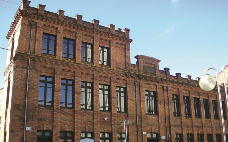 Fachada del Museo de la Siderurgia de Asturias en Langreo, construida en ladrillo visto rojizo con amplios ventanales de estilo industrial enmarcados en hierro; en primer plano se aprecia una farola de forja bajo un cielo despejado.