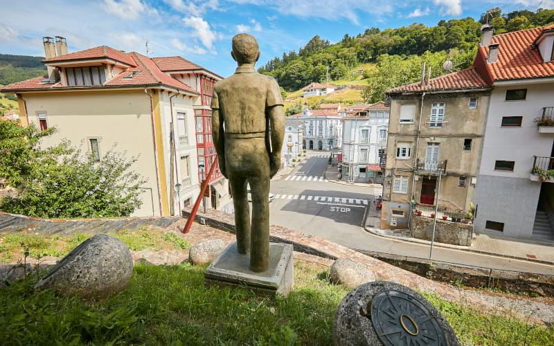 Die Skulptur ist eine Hommage an die Auswanderer von Allande und befindet sich auf einer Anhöhe, von der aus man einen Teil des Stadtzentrums mit traditionellen Häusern und bewaldeten Hügeln im Hintergrund sehen kann.
