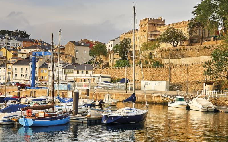 Embarcações atracadas no porto de Figueras, em Castropol, com o palácio da família Pardo Donlebún e as casas do centro da cidade a elevarem-se sobre o cais.