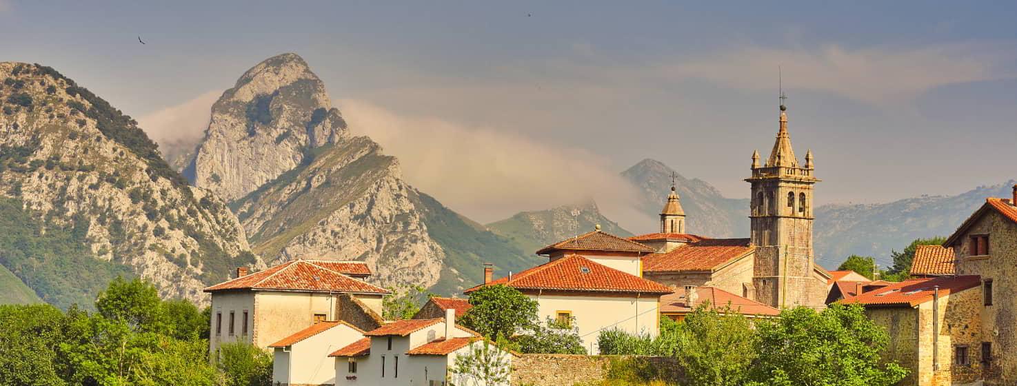 Vista de Alles, capital de Peñamellera Alta, pequeño pueblo de montaña con casas blancas de tejados rojos, en el que destaca la iglesia con una torre. Está rodeado bosques y montañas, en las que se combina los colores gris o plata de la caliza típica de esta zona con el verde de sus praderas y el azul del cielo.