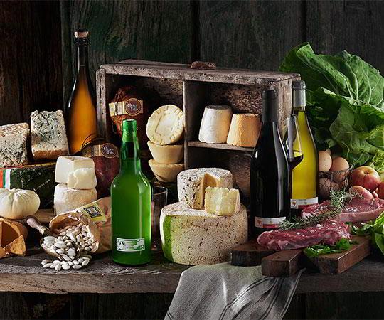 Photo of a still life of Asturian products. Various types of Asturian cheeses, meat, beans, sausages, cider and wine from Cangas.