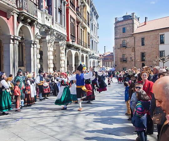 A group of people dance in the regional costume of Asturias in the centre of the street, while the public forms a corridor on both sides in Avilés.