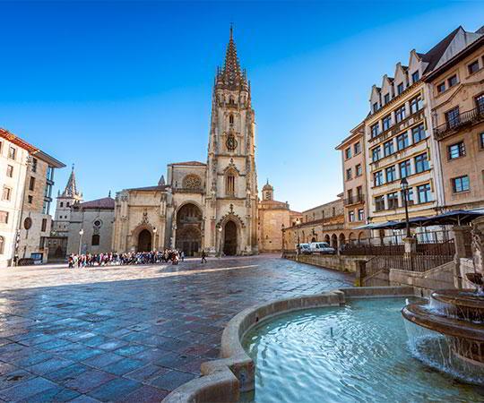 Photo of the façade of the cathedral of El Salvador in Oviedo/Uviéu and its square with the fountain in the foreground.