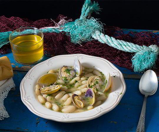 A still life photo featuring a plate of beans with clams in the foreground
