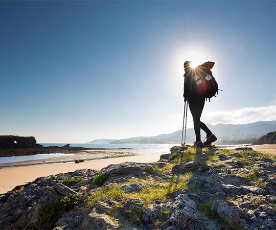 Photo of a pilgrim walking the Camino de Santiago along the coast, passing through the municipality of Colunga. In the foreground, a Camino sign is visible
