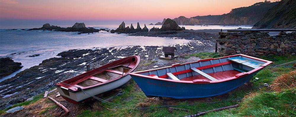 Panoramic view of Gueirúa beach in the municipality of Cudillero with two wooden boats in the foreground.