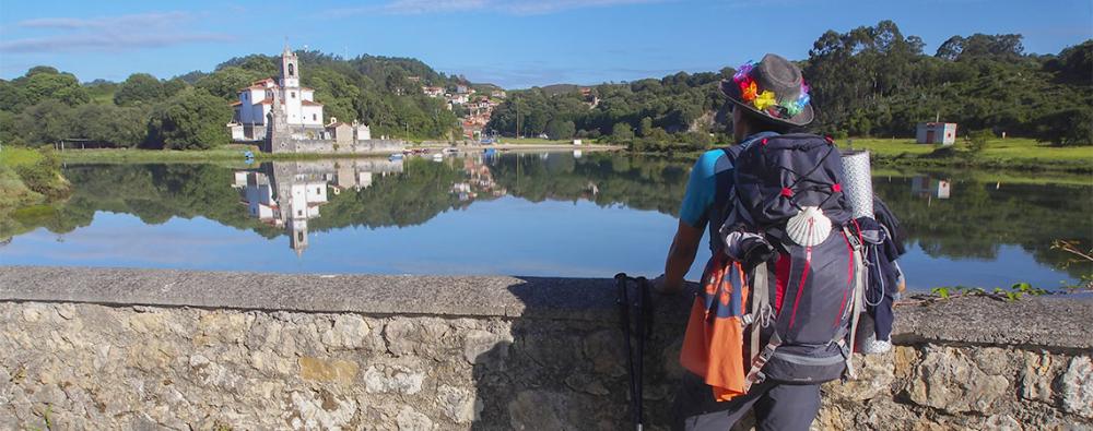 Image of a pilgrim in the foreground looking at the church of Nuestra Señora de los Dolores in Barru (Llanes).