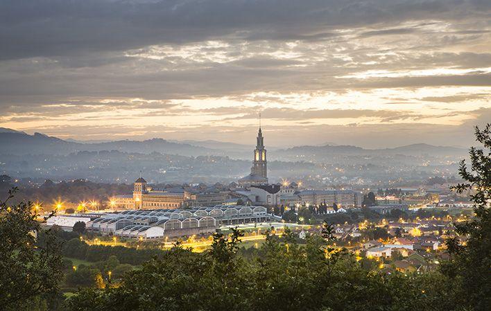 Universidad Laboral de Gijón in der Abenddämmerung, Blick von der Rückseite mit dem beleuchteten Museumsgebäude und einem bewölkten Himmel zwischen Dunkelheit und Abendlicht.