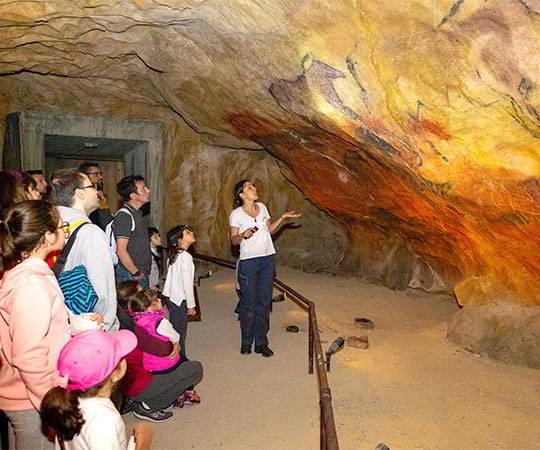 Image of the interior of the Cueva de Cuevas in the Prehistoric Park with people listening to the guide's explanations.