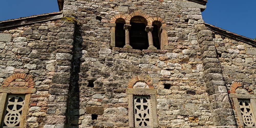 Exterior architecture of San Pedro de Nora, with the main window with three arches and the small side windows with latticework standing out.